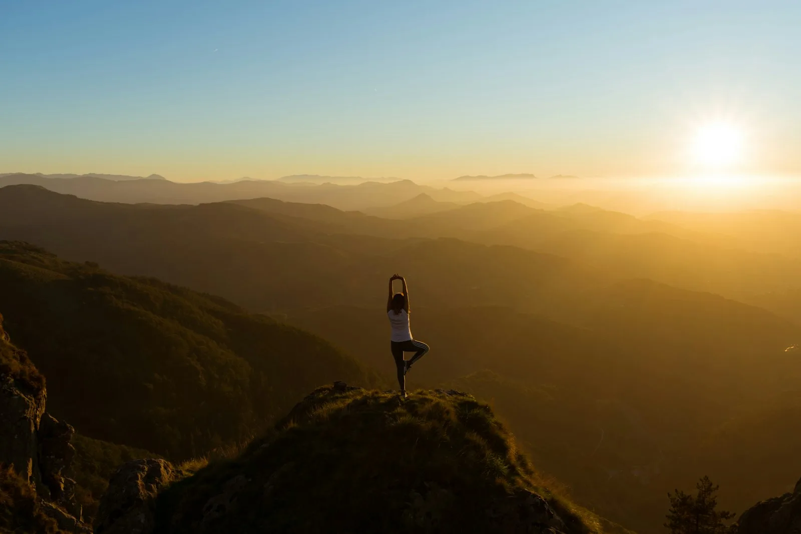A lone figure in silhouette on a ridge at sunrise, arms resting in stillness